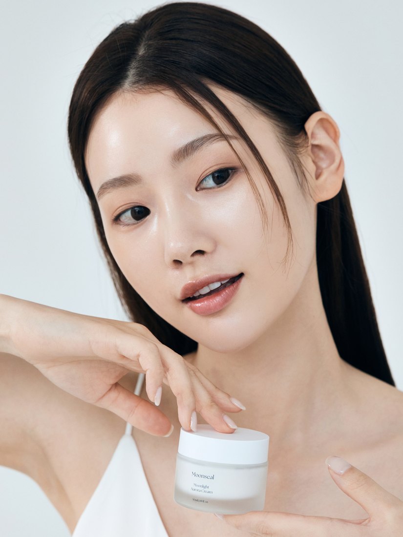 Rostro con piel luminosa sosteniendo la crema Moonseal Moonlight Aurora